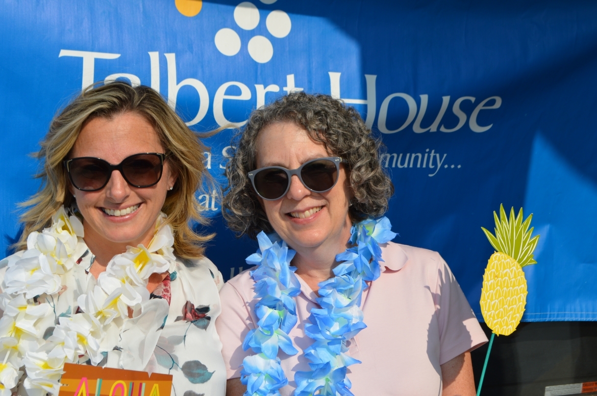 Two people wearing flower necklaces and sunglasses in front of Talbert House sign